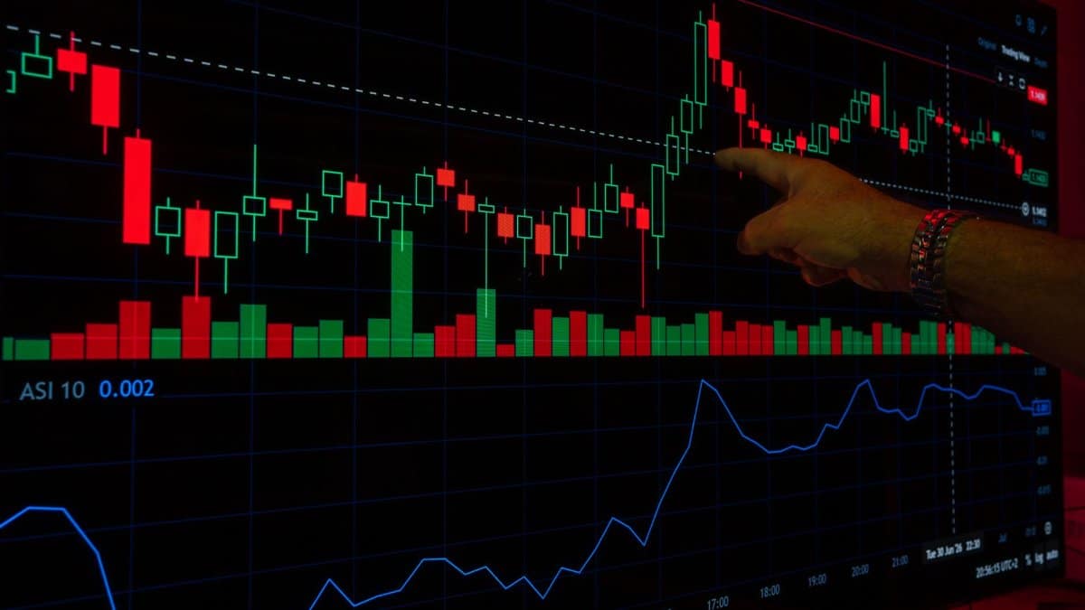 A hand points at a stock market graph on a digital screen, highlighting financial trading trends.