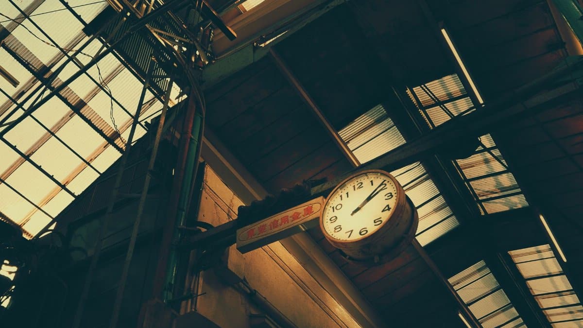 Low angle view of a vintage clock in a Japanese railway station with industrial structures overhead.