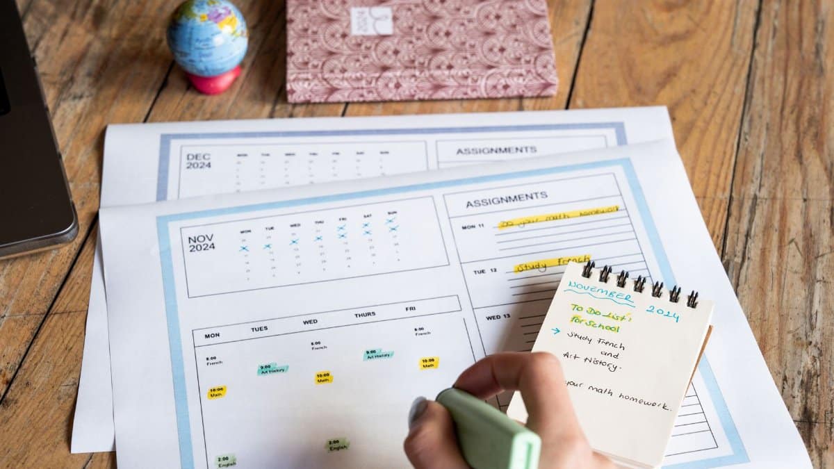 Person planning tasks with a calendar and notepad on a wooden table.