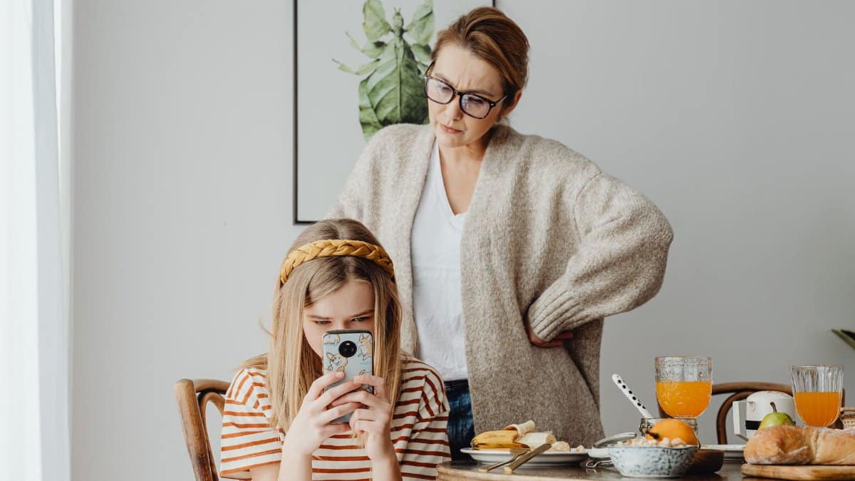 A mother looking at her daughter absorbed in a phone during breakfast. Modern family dynamics.