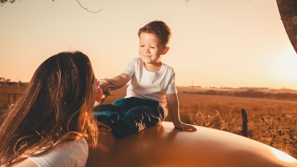 A mother and child share a tender moment in a sunny field during sunset, capturing a sense of warmth and togetherness.