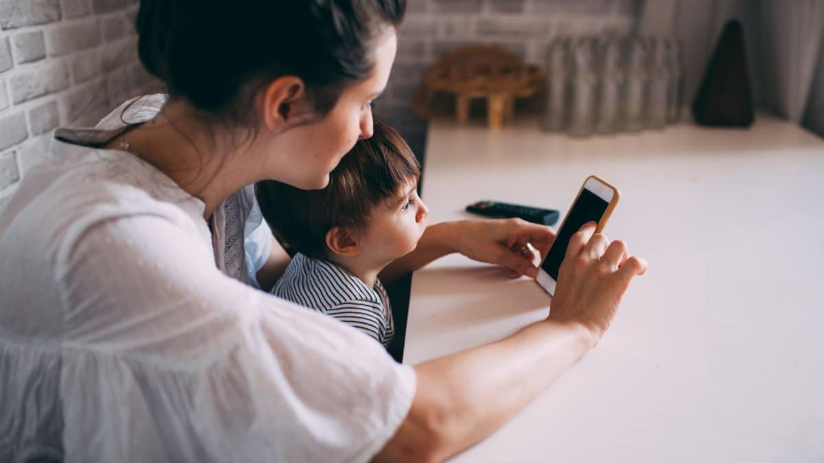 A woman and child interacting with a smartphone at home, highlighting technology and family bonding.