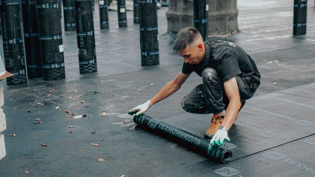 Construction worker applies waterproof membrane on rooftop for protection against weather elements.