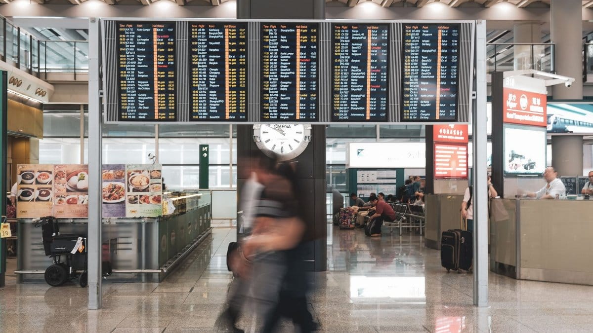 Blurred motion of travelers in a modern airport terminal with departure screens and a prominent clock.