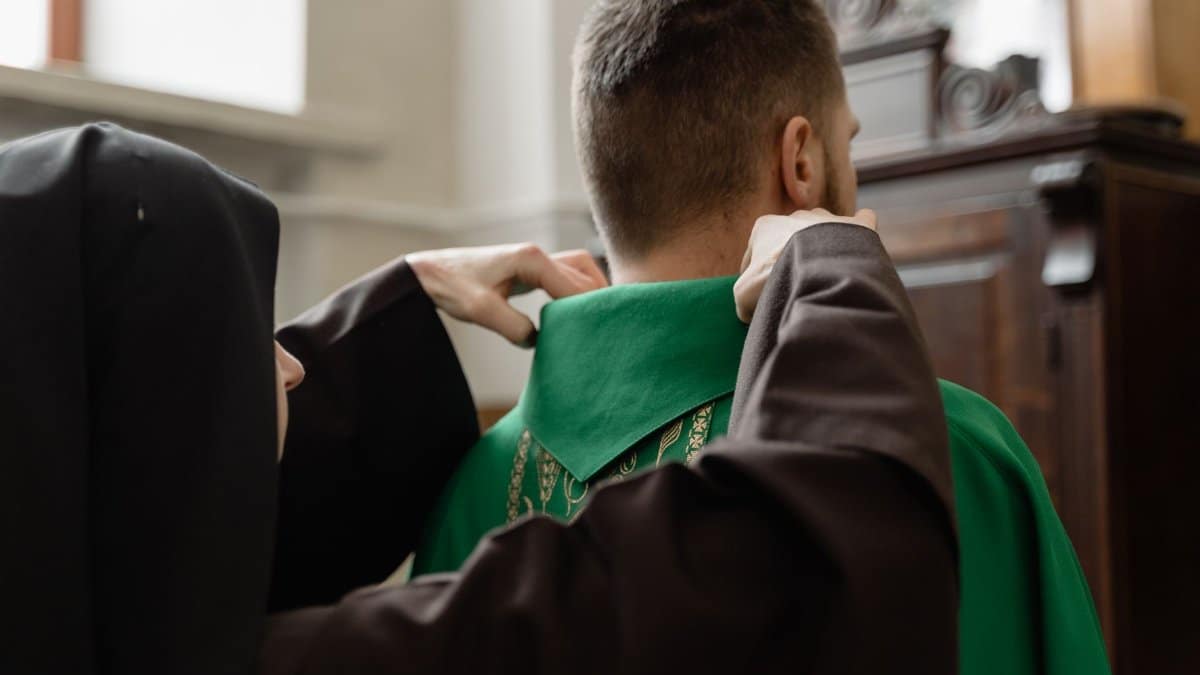 A nun assists a priest by adjusting his robe in preparation for a religious service inside a church.