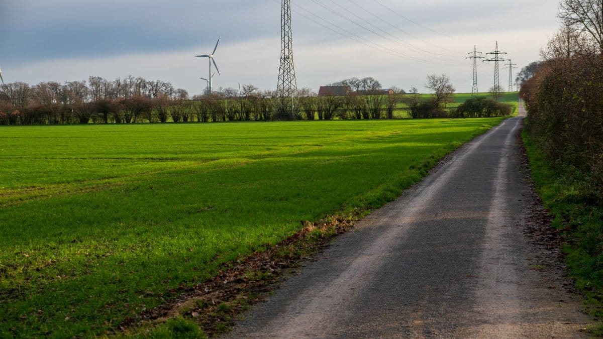 Scenic rural pathway bordered by green fields and wind turbines under a cloudy sky.