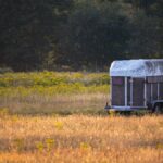 A scenic rural landscape featuring an abandoned trailer in a sunlit meadow.