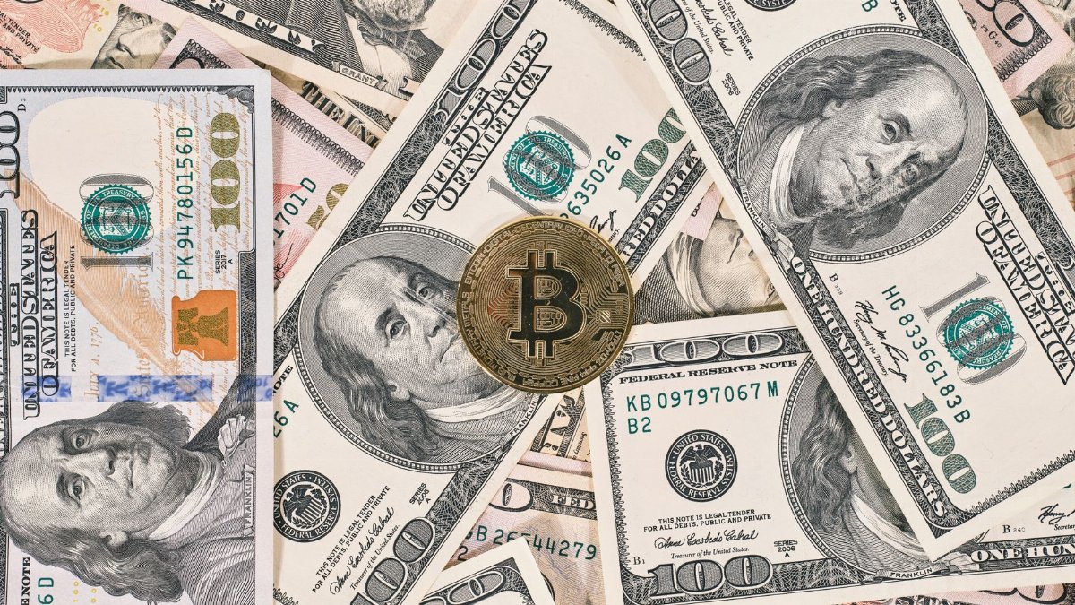 Bitcoin coin resting on a background of various US dollar bills, symbolizing the contrast between traditional and digital currency.