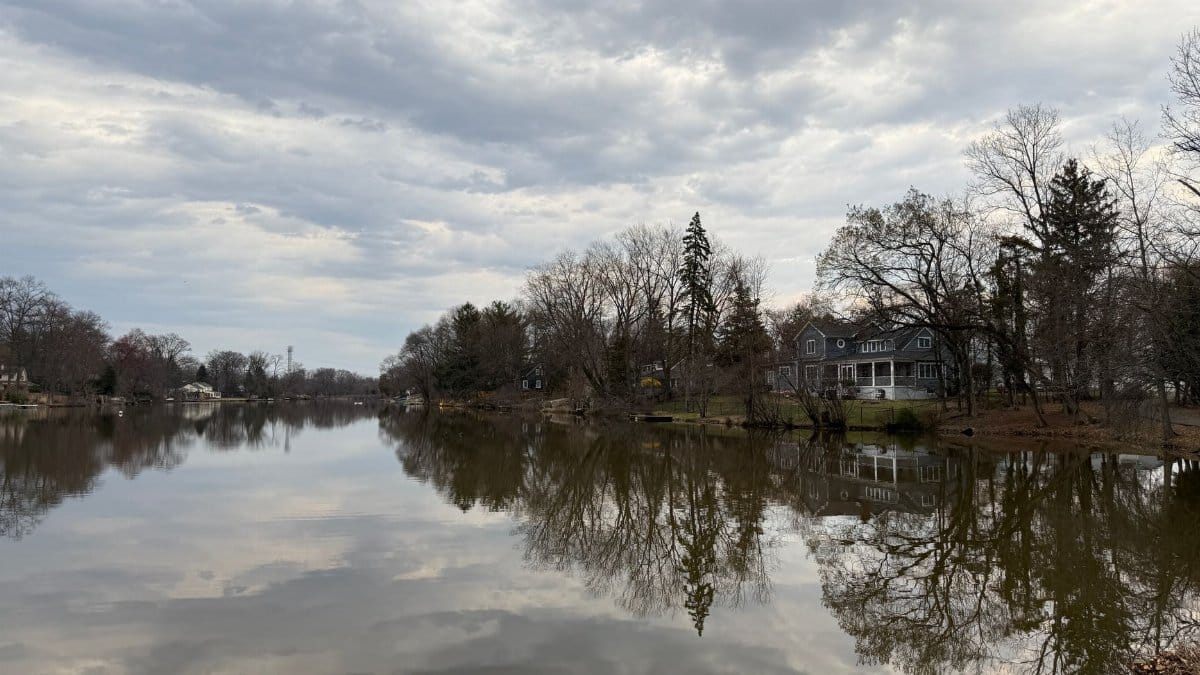 A serene view of a lake with house reflections and overcast skies.