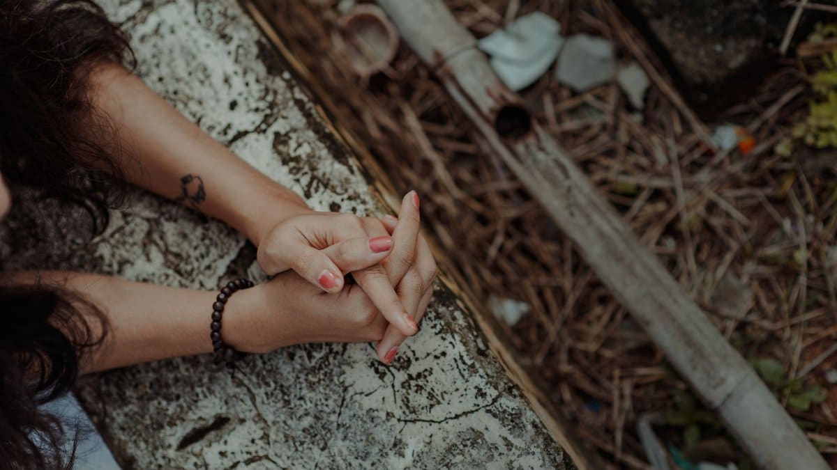 Close-up shot of hands with bracelet and tattoo on weathered surface, showcasing earthy tones.