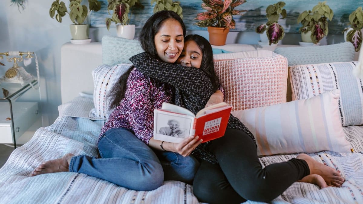 A loving mother and daughter reading a book together in a cozy home setting, embracing and smiling.