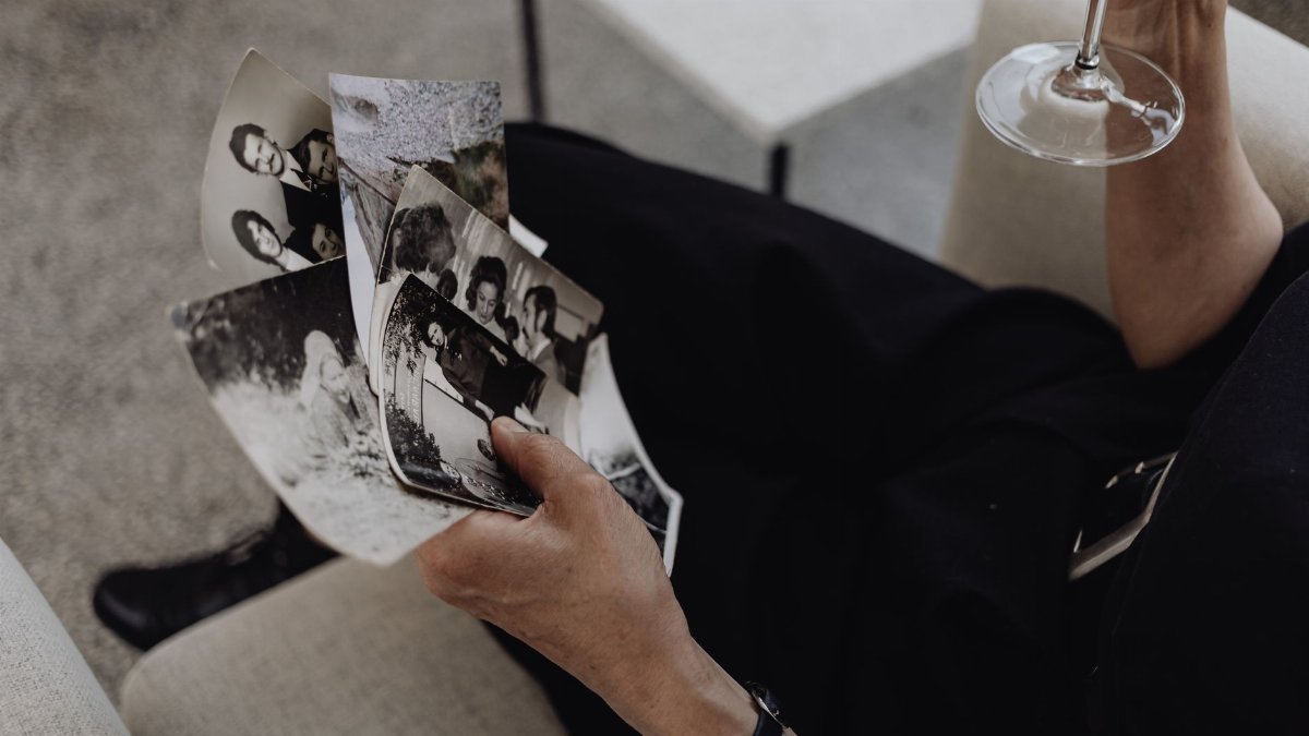 A person reflecting on memories while holding photographs and a wine glass.