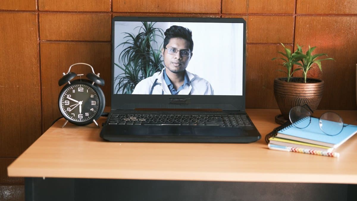 A home office desk with a laptop showing a virtual doctor, ideal for online consultation themes.