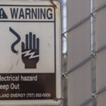 Close-up of a warning sign for electrical hazards on a chain-link fence.