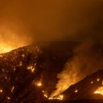 Intense wildfire blazing through mountains in California at night, creating a dramatic scene.