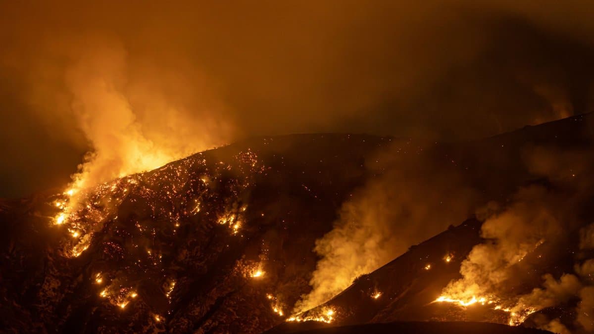 Intense wildfire blazing through mountains in California at night, creating a dramatic scene.