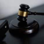 High angle of shiny wooden ceremonial mallet with golden detail placed on judge tale near documents folders