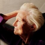 Captivating portrait of a smiling senior woman with gray hair enjoying sunlight indoors.