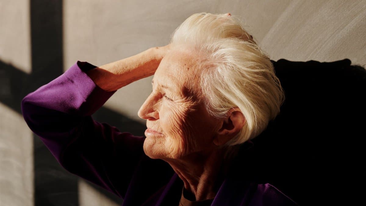 Captivating portrait of a smiling senior woman with gray hair enjoying sunlight indoors.