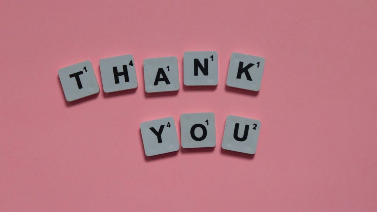 Scrabble tiles forming 'Thank You' on a pink background, ideal for gratitude concepts.