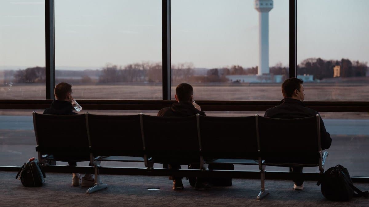 People sitting in airport terminal, watching runway scenes through large windows.