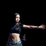 Fashionable young woman striking a pose in a studio with a dark backdrop, showcasing modern style.