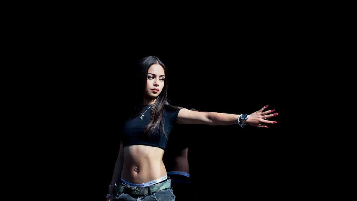 Fashionable young woman striking a pose in a studio with a dark backdrop, showcasing modern style.