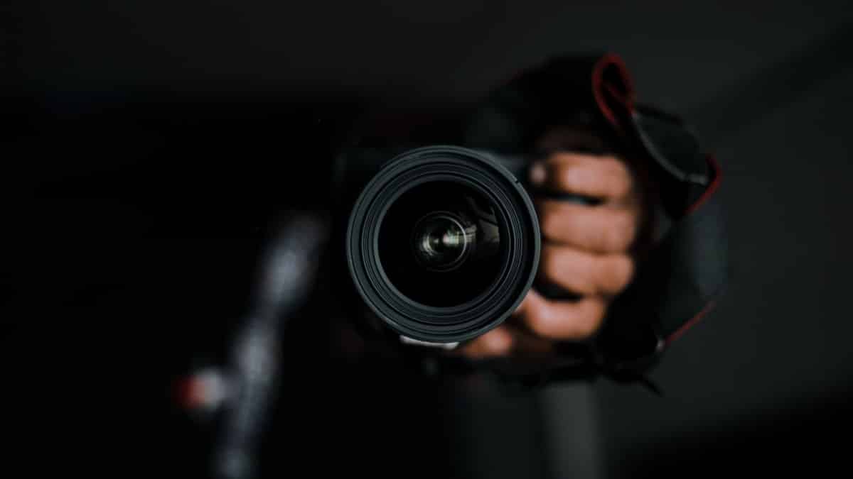 Close-up of a hand holding a DSLR camera lens, focusing on the intricate lens details.