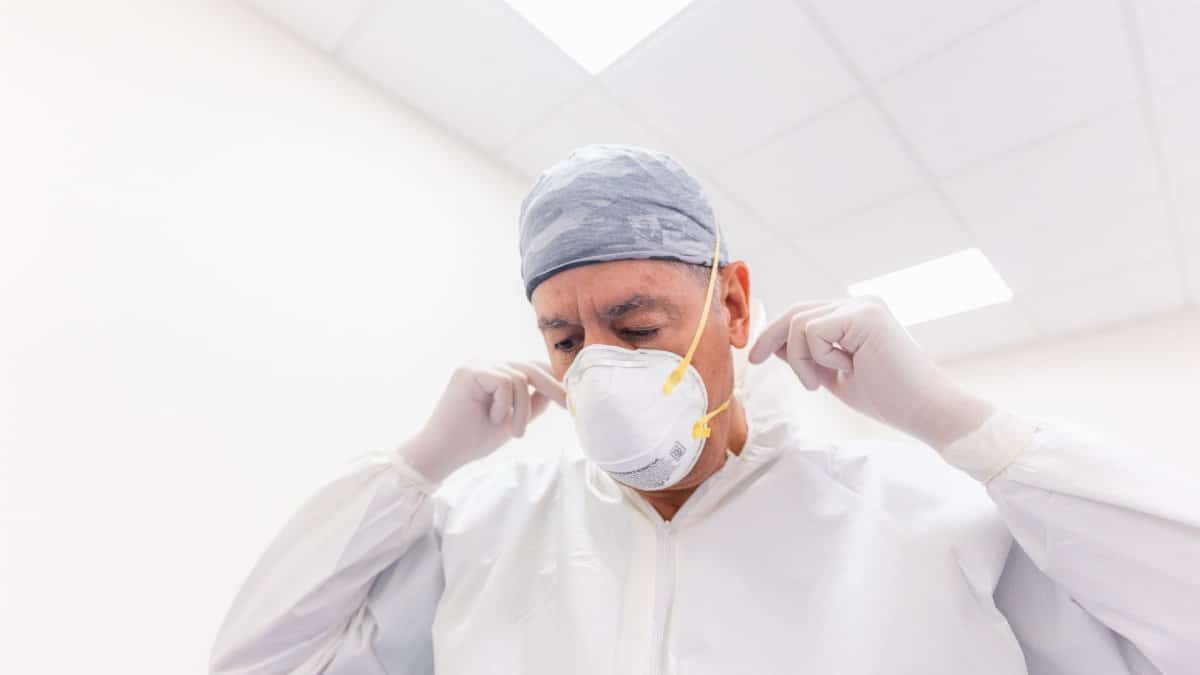 Male healthcare professional adjusting face mask and PPE in a hospital setting.