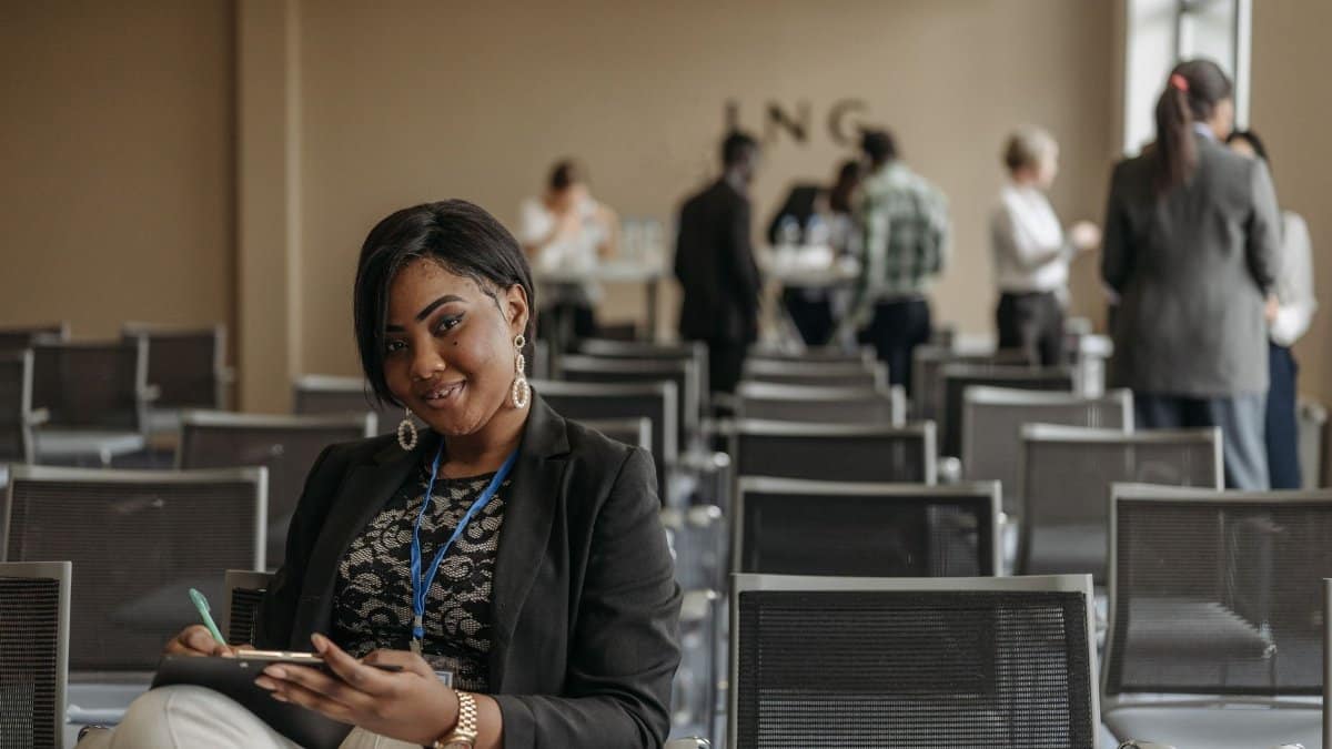 Businesswoman smiling while taking notes at a conference room event. Bright and professional setting indoors.