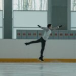 A figure skater performs an impressive leap on an indoor ice rink.