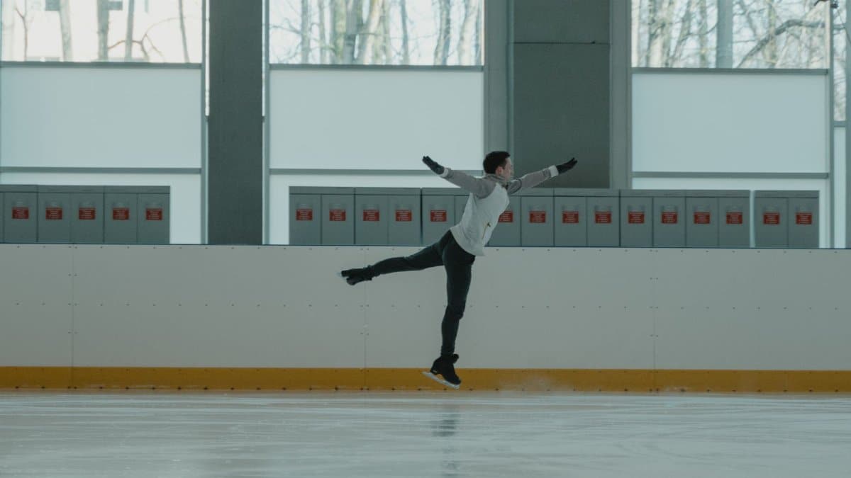 A figure skater performs an impressive leap on an indoor ice rink.