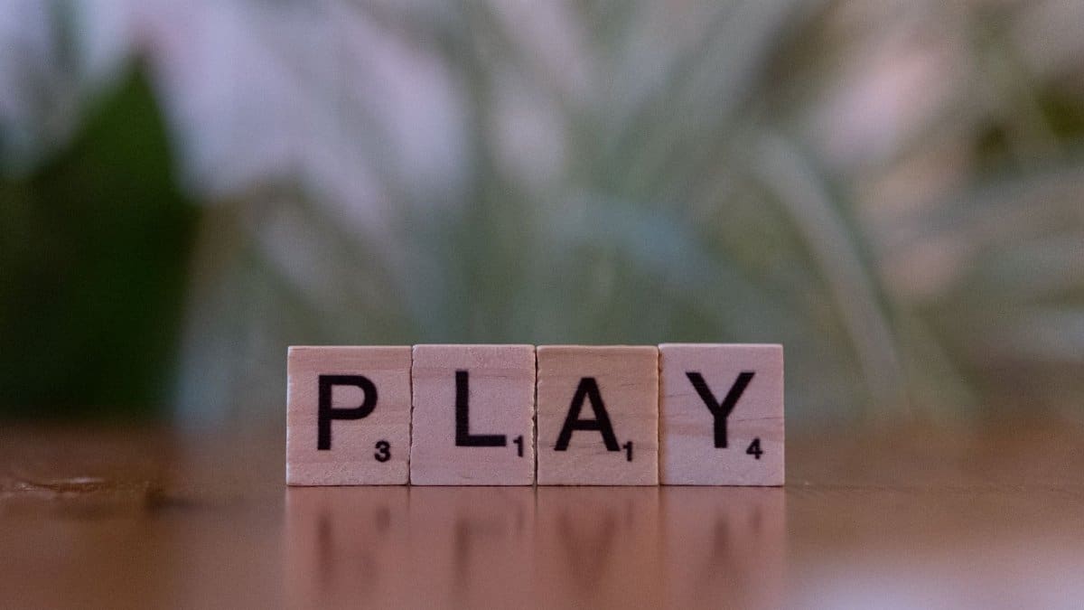 Close-up of wooden Scrabble tiles spelling 'PLAY' on a table with a soft focus background.