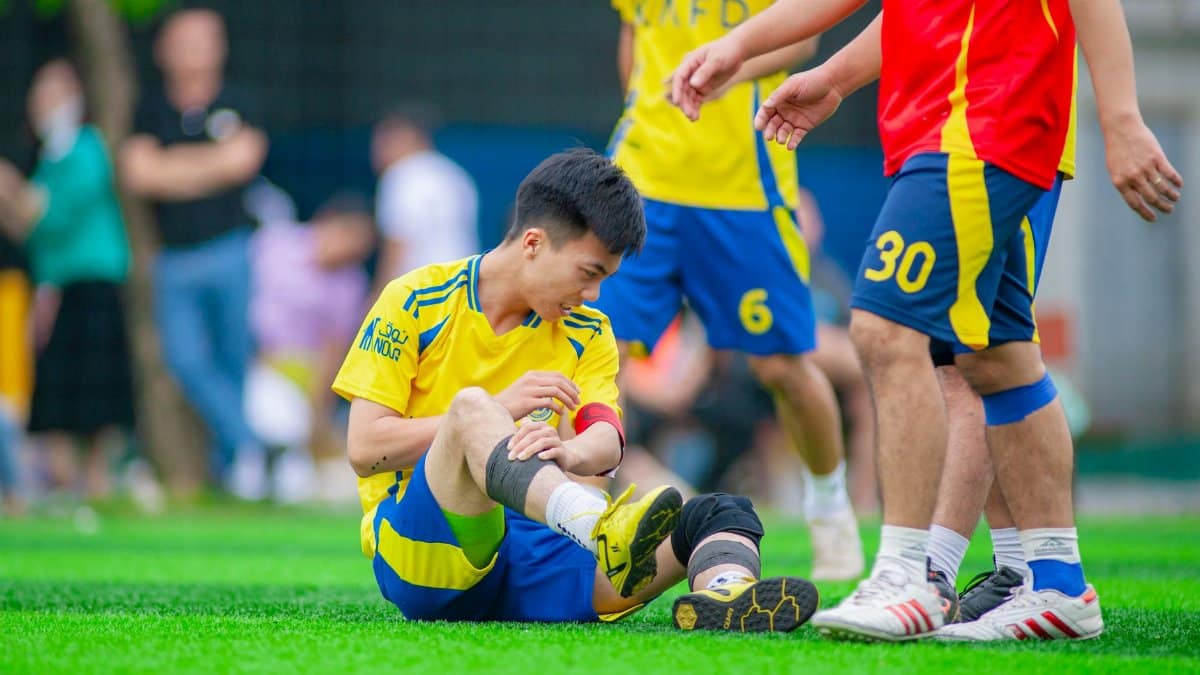 Amateur soccer player sitting on grass, nursing a leg injury during game in Hanoi, Vietnam.