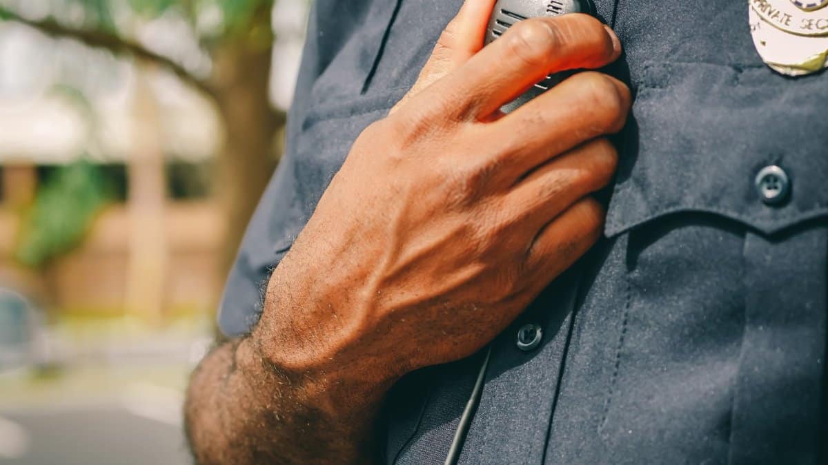 Close-up of police officer holding a radio outdoors, showcasing communication tools in law enforcement.