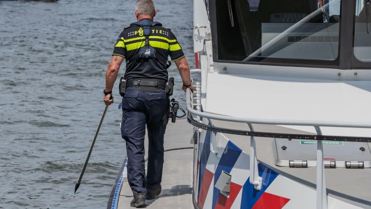 A Dutch police officer walking on a boat deck, performing patrol duties on the water.