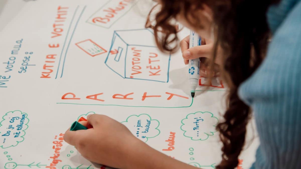 Child drawing colorful illustrations and text on paper, engaging in creative school activity.