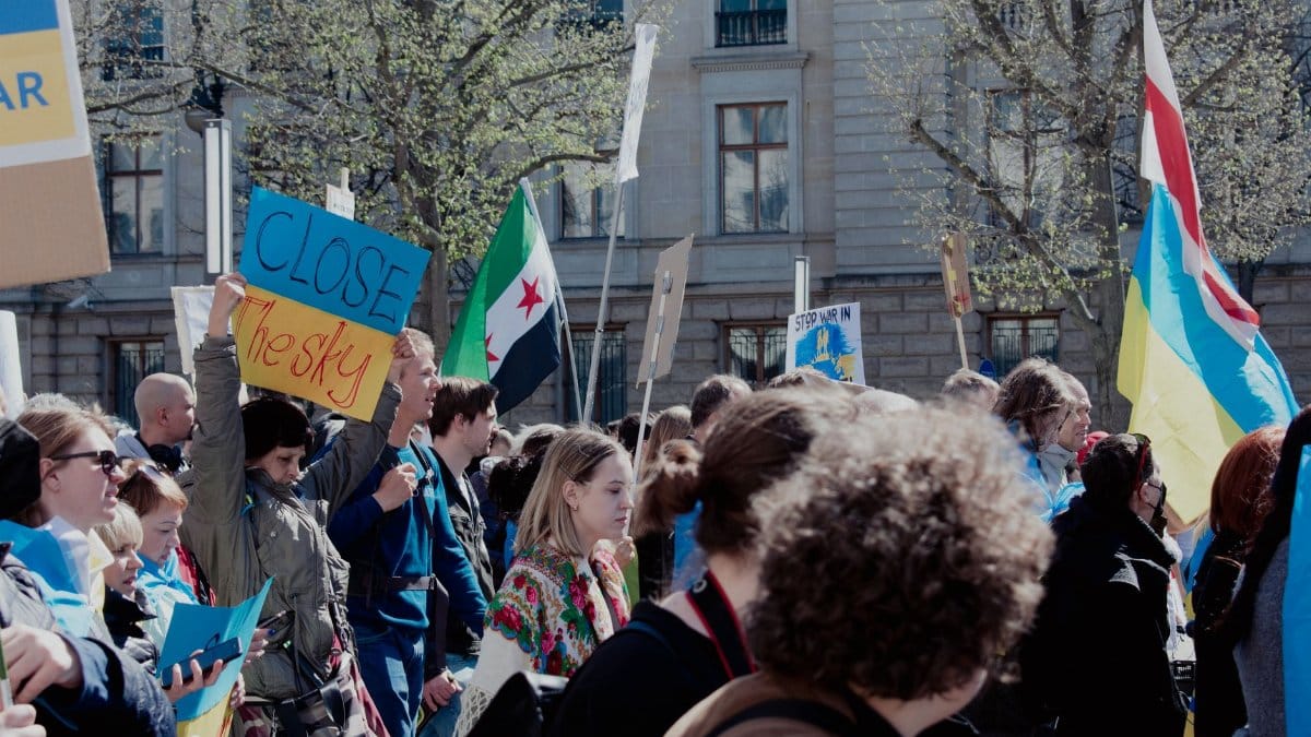 Crowd of activists protesting in Berlin with various banners and flags, advocating for change.