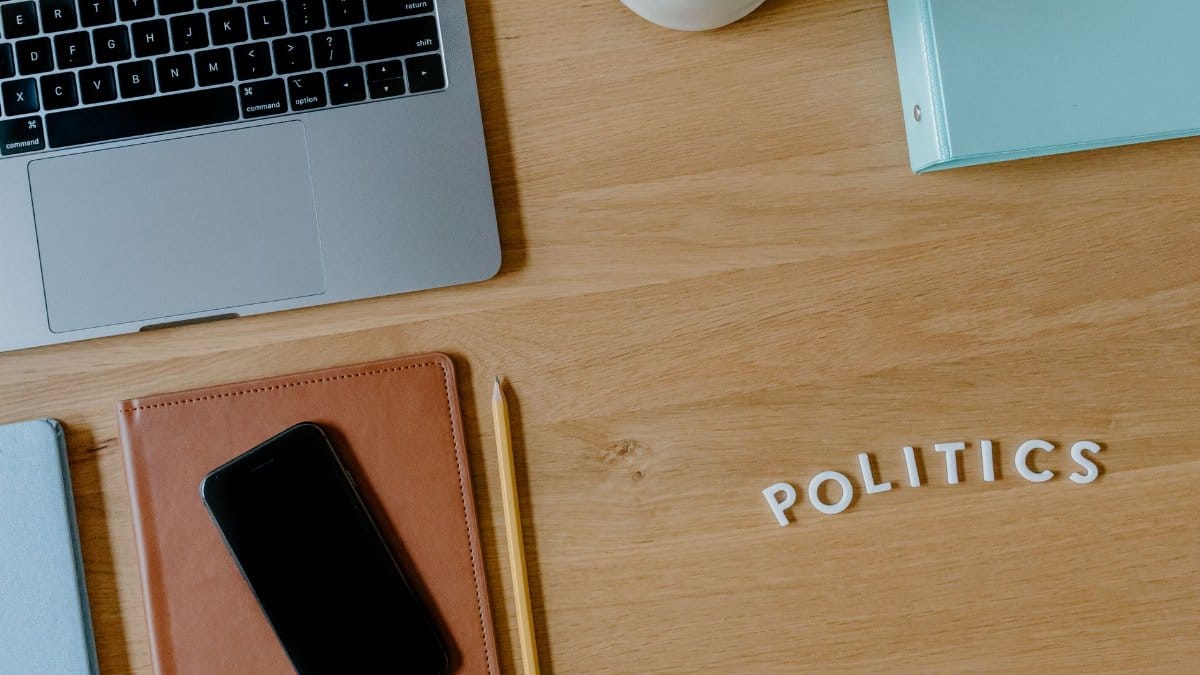 A top view of a workspace featuring a laptop, smartphone, and 'politics' text on a wooden desk.