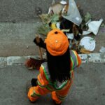 A street cleaner in an orange uniform sweeps debris from the roadside, ensuring cleanliness.