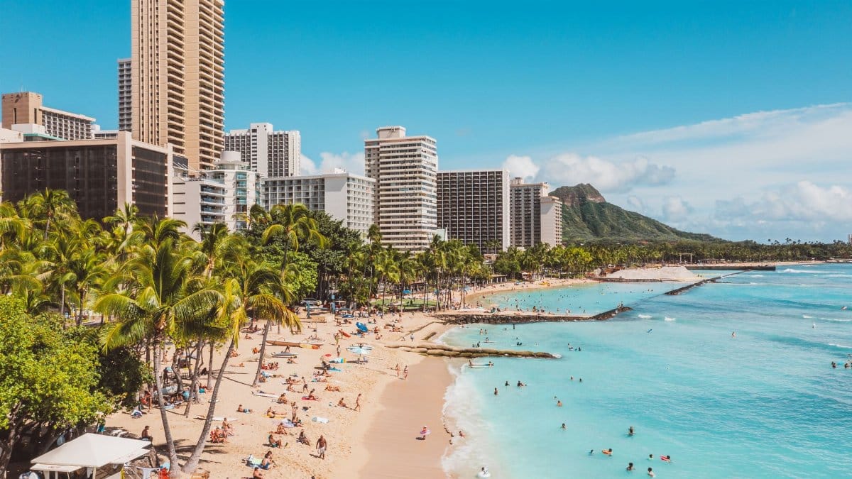 A bustling Waikiki Beach scene with skyscrapers and Diamond Head in the background, highlighting a popular travel destination.