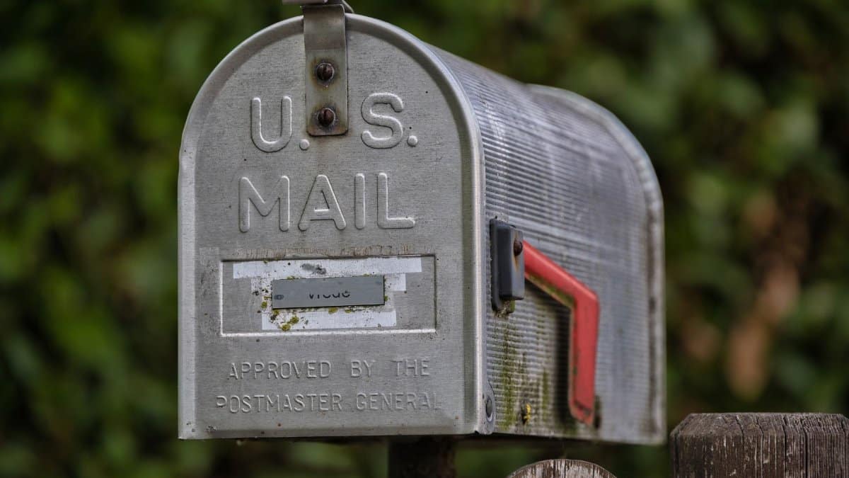 Close-up of a classic U.S. mailbox on a rustic wooden post, outdoors.