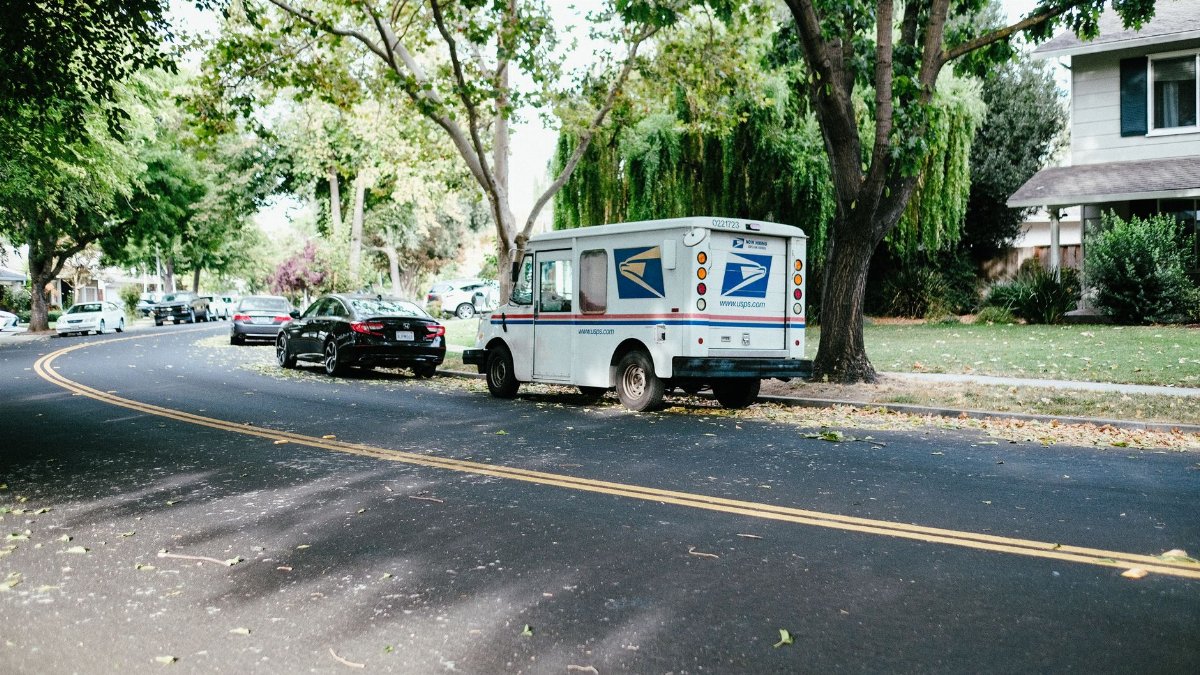 A postal delivery van parked on a tree-lined suburban street, showcasing daily mail service.