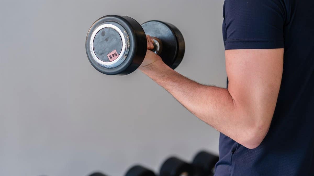Close-up of a man lifting a dumbbell in a gym, emphasizing fitness and strength training.