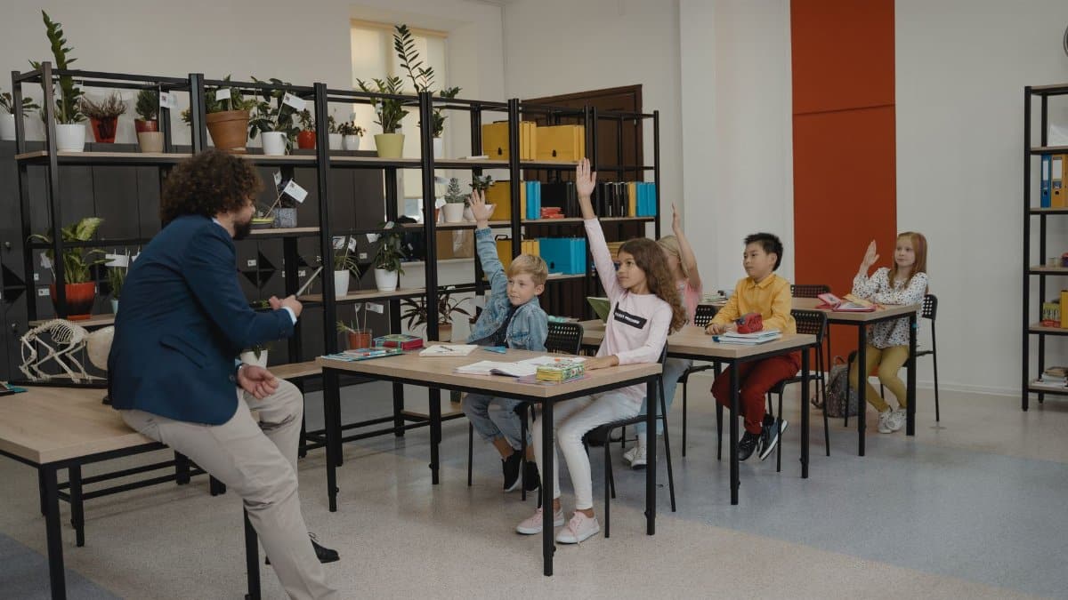 Students actively participating by raising hands in a modern classroom with attentive teacher and organized environment.