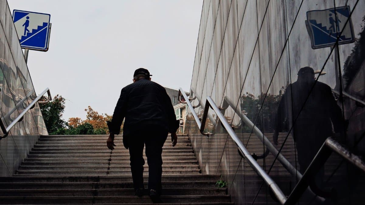 A person climbing outdoor subway stairs with reflections on a wall, emphasizing urban life.