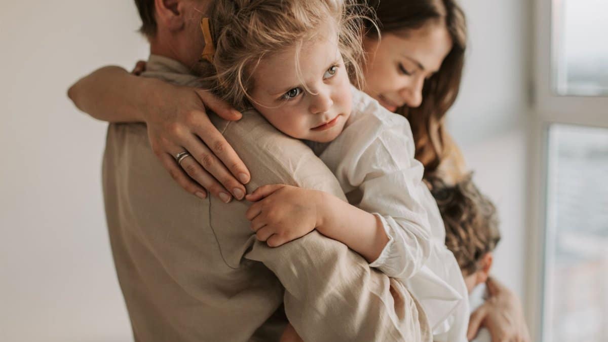 A young family shares a tender embrace inside a cozy home setting, highlighting love and togetherness.