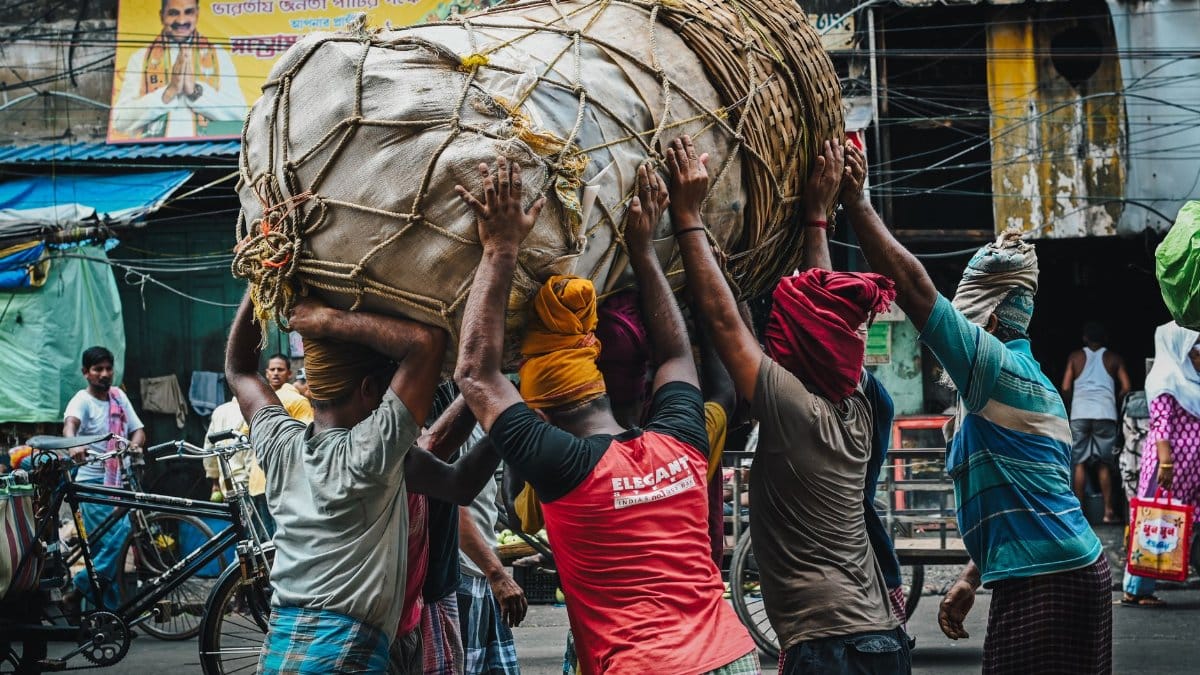 A group of men working together to lift a massive basket in a busy Kolkata street.