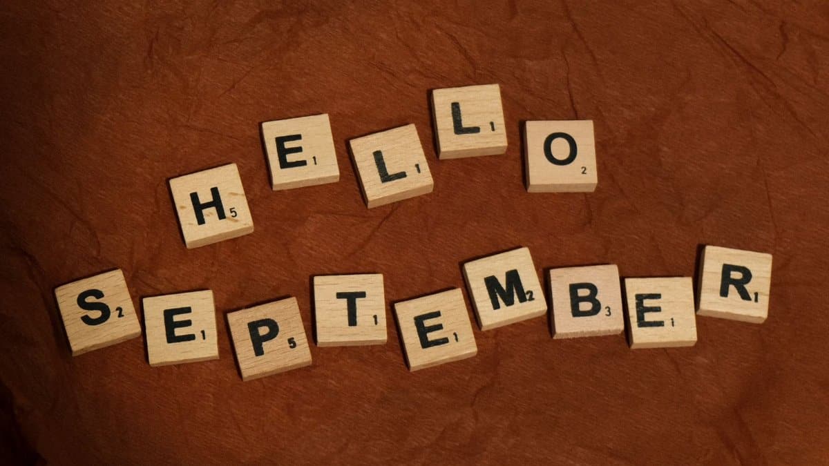 Wooden letter tiles arranged to say 'Hello September' on a textured brown background.