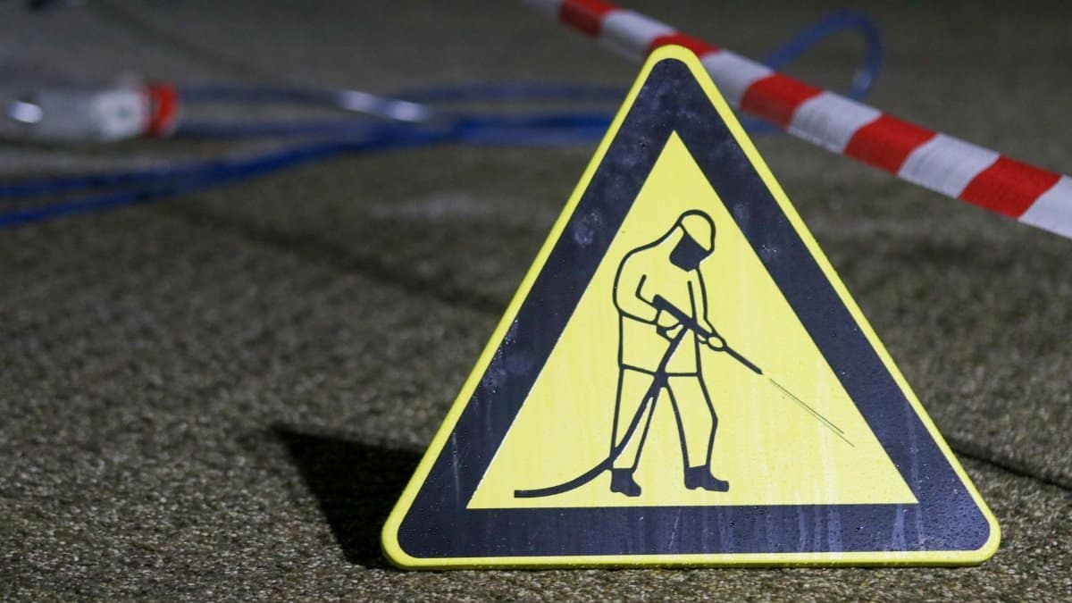 Yellow caution sign depicting pressure washing in a night setting with safety barriers.